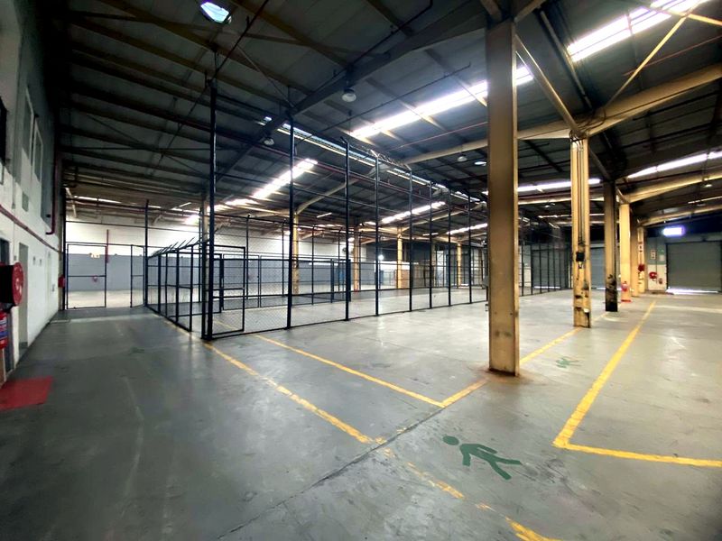 Spacious industrial warehouse featuring high ceilings, concrete flooring, steel structural columns, and internal chain-link partitioned areas suitable for storage or manufacturing operations.