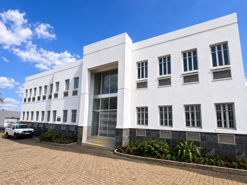 Front elevation of a modern industrial building featuring a paved driveway, stone-clad base, and symmetrical multi-pane windows with integrated ventilation louvers.