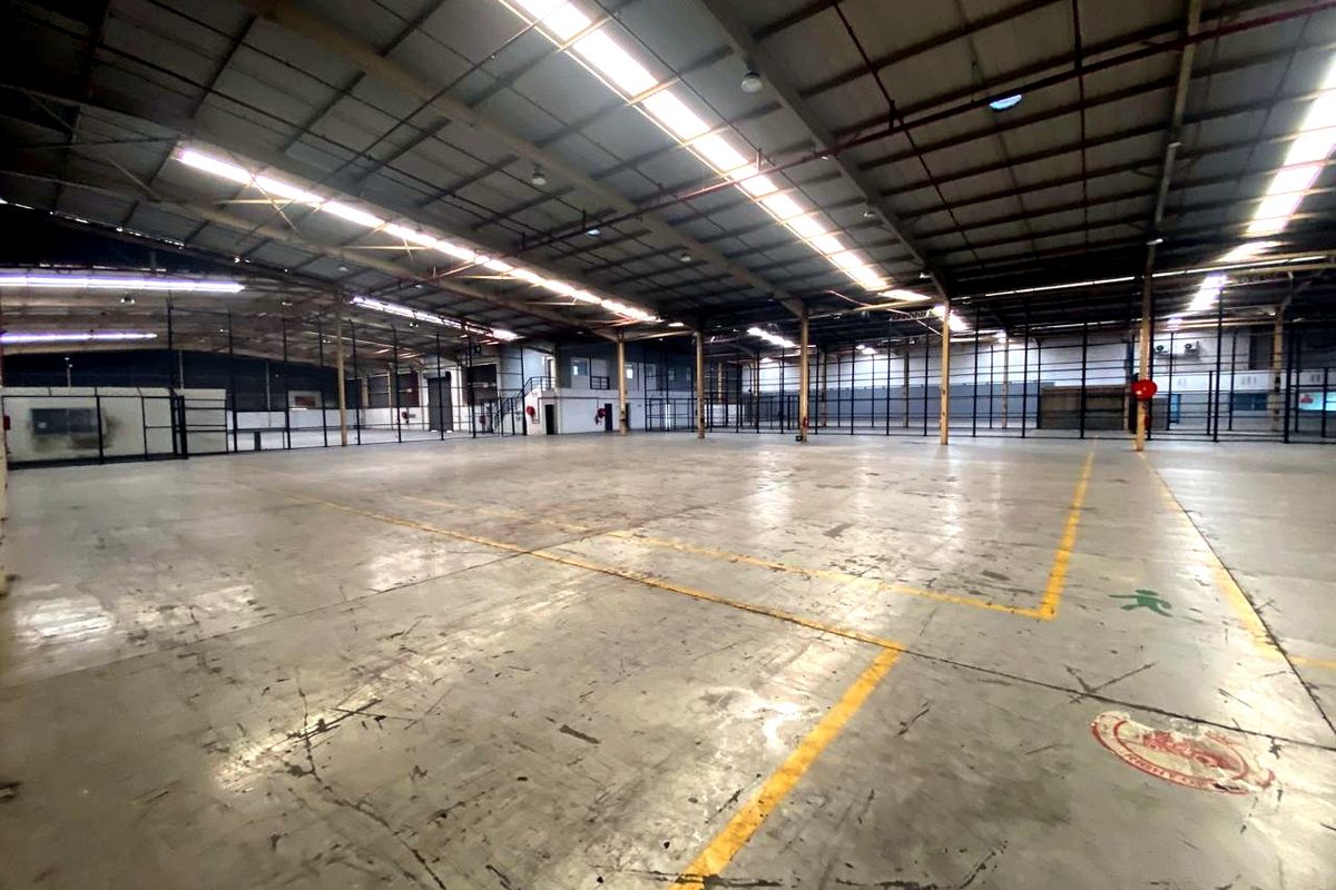 Expansive industrial warehouse space featuring high ceilings, concrete flooring, integrated skylights, and robust steel structural framing, suitable for various commercial or storage operations.