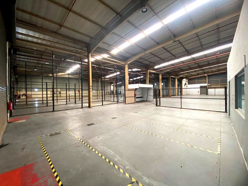 Spacious industrial warehouse featuring high ceilings with skylights, concrete flooring, fire sprinkler system, and partitioned storage areas with chain link fencing.