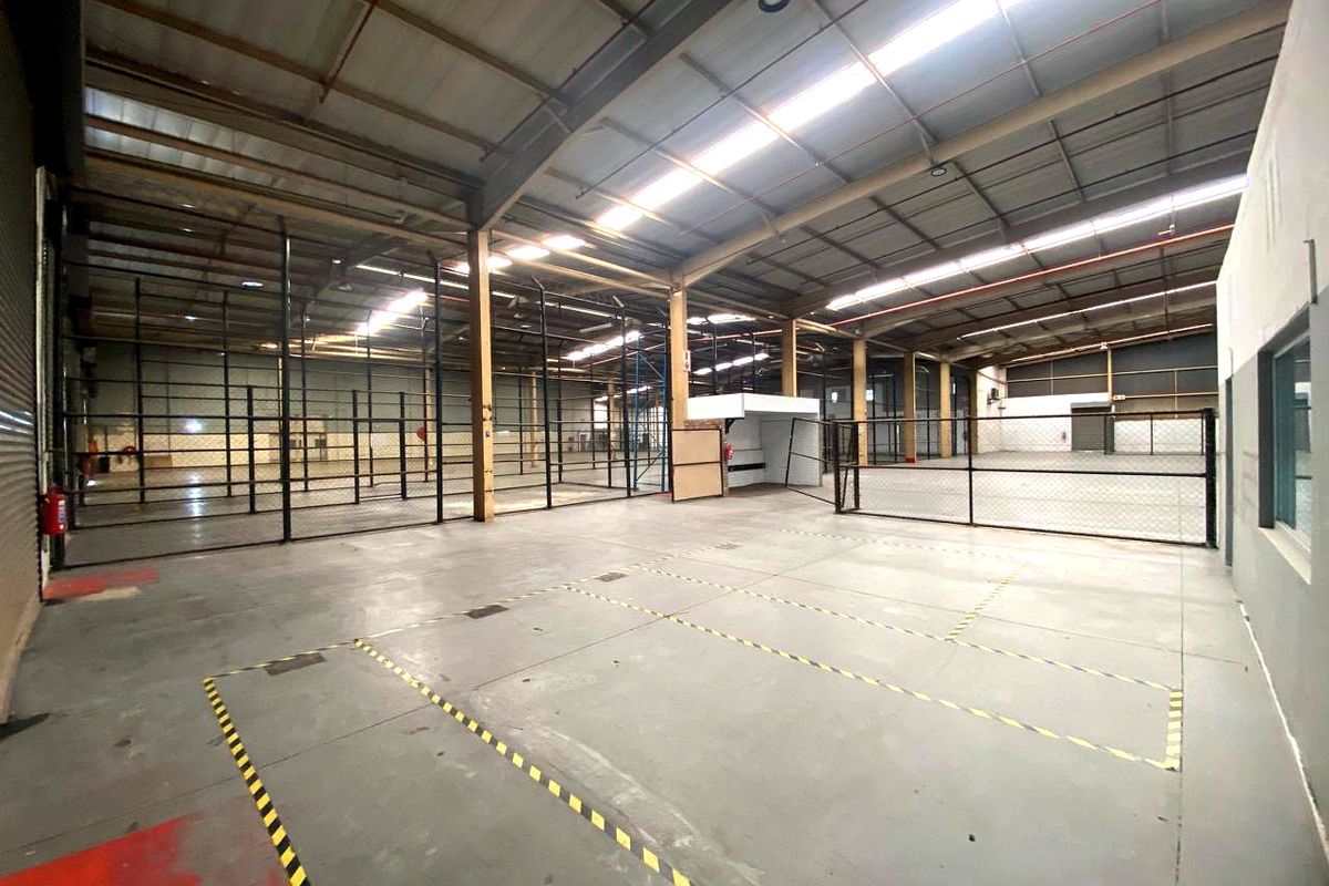 Spacious industrial warehouse featuring high ceilings with skylights, concrete flooring, fire sprinkler system, and partitioned storage areas with chain link fencing.