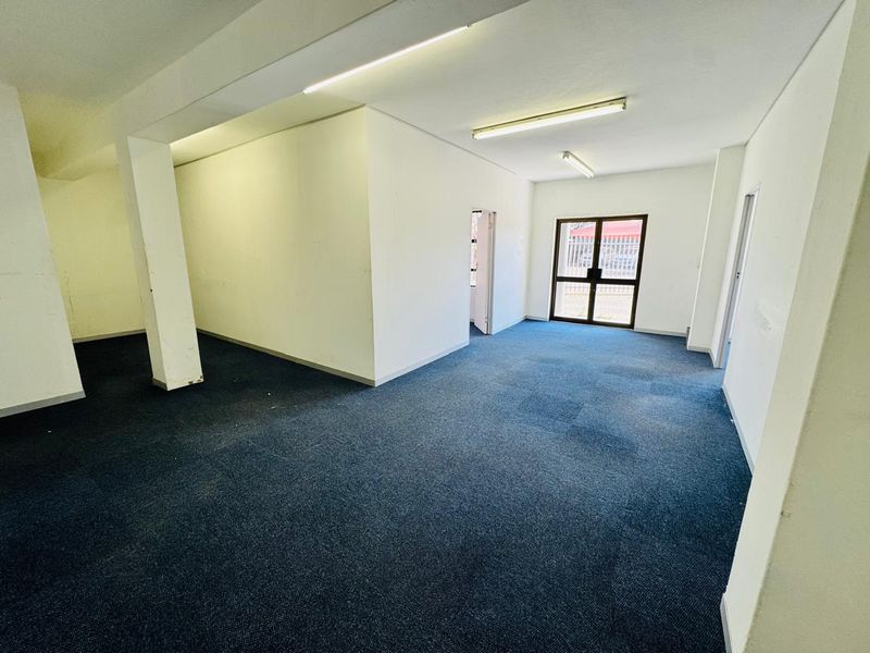 An empty, open-plan office space featuring blue carpeting, structural columns, and fluorescent lighting, providing a blank canvas for professional use.