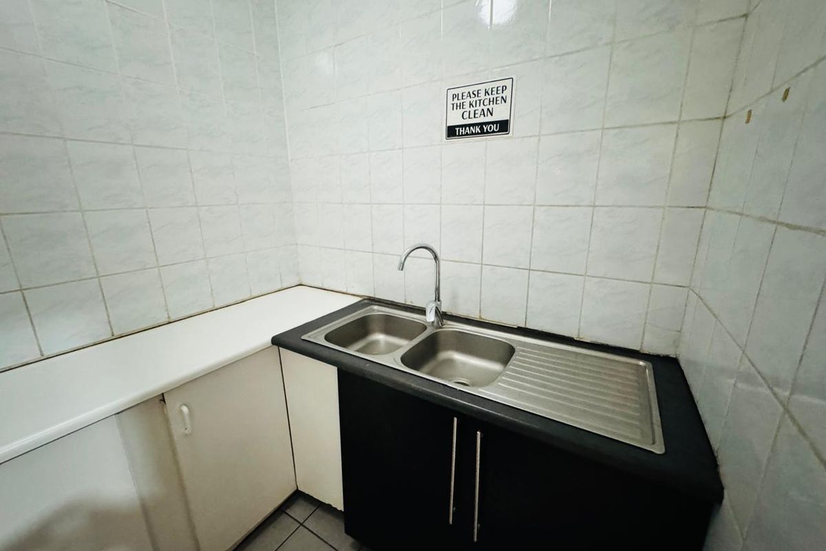 A functional office kitchenette featuring a stainless steel double sink, tiled backsplash, and built-in cabinetry with laminate countertops.