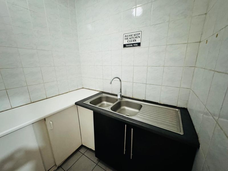 A functional office kitchenette featuring a stainless steel double sink, tiled backsplash, and built-in cabinetry with laminate countertops.