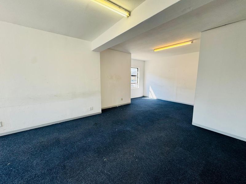 An empty office space featuring blue carpeting, fluorescent lighting, and neutral walls, providing a blank canvas for professional workspace customization.