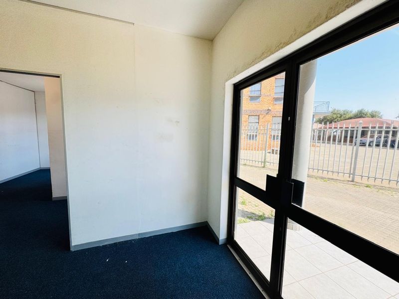 An empty office space featuring dark carpeting, white walls with visible wear, and a large glass door providing exterior access.