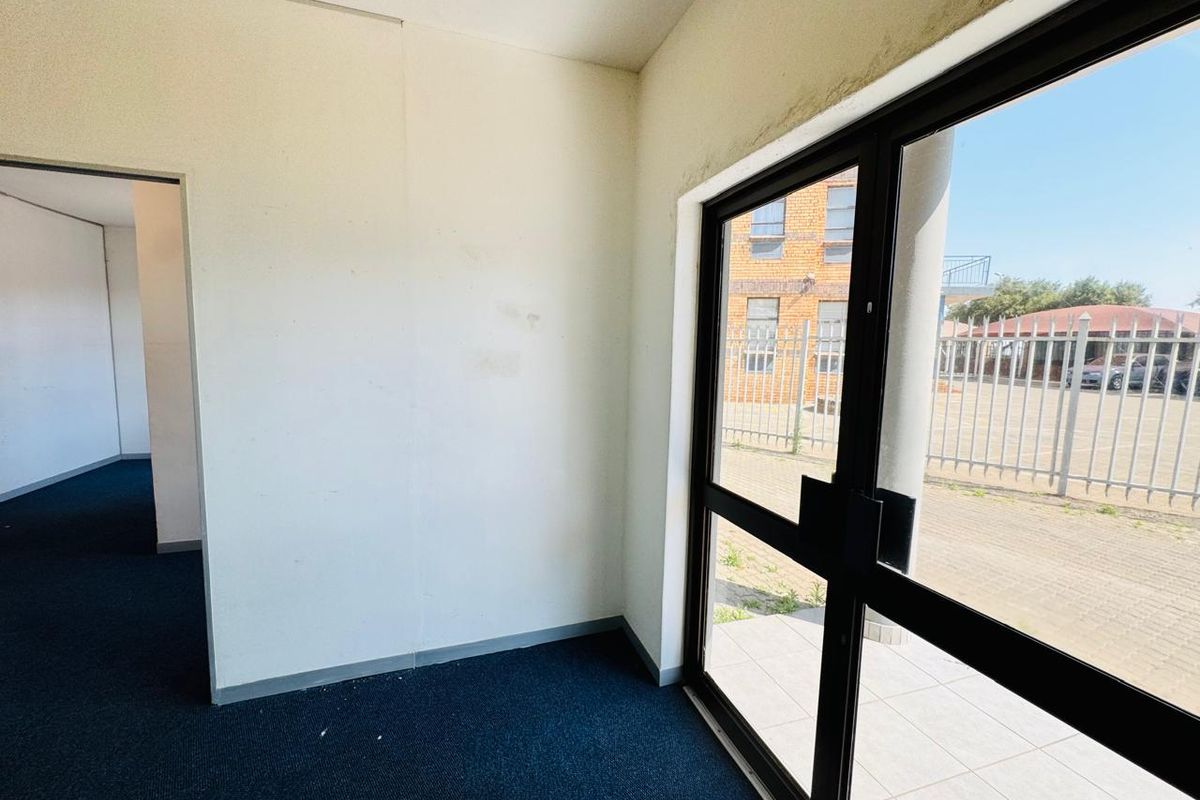 An empty office space featuring dark carpeting, white walls with visible wear, and a large glass door providing exterior access.
