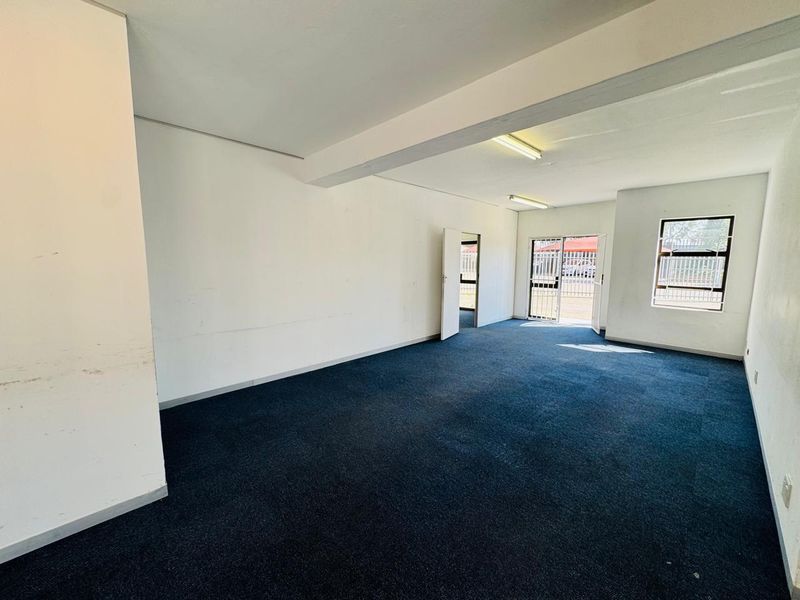 An empty, open-plan office space featuring blue carpeting, fluorescent lighting, and secure access with burglar bars on the windows.