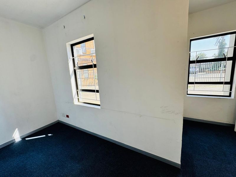 An empty office space featuring dark carpeting, white walls with visible scuff marks, and windows fitted with security bars.