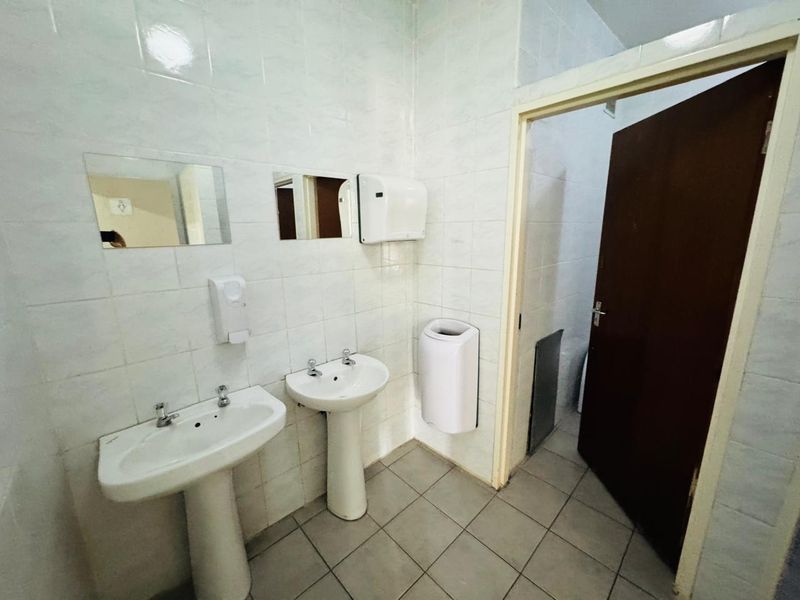 A functional office bathroom featuring dual pedestal wash basins, tiled walls and flooring, and essential sanitary fixtures.