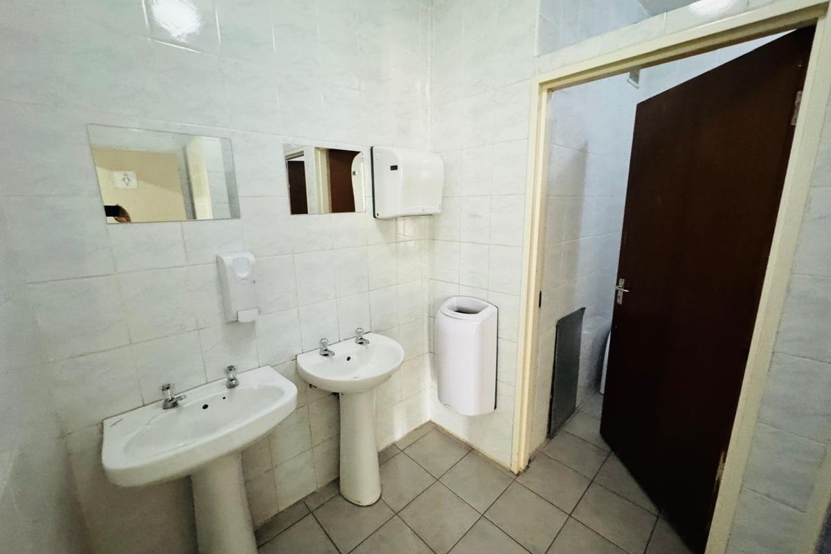 A functional office bathroom featuring dual pedestal wash basins, tiled walls and flooring, and essential sanitary fixtures.