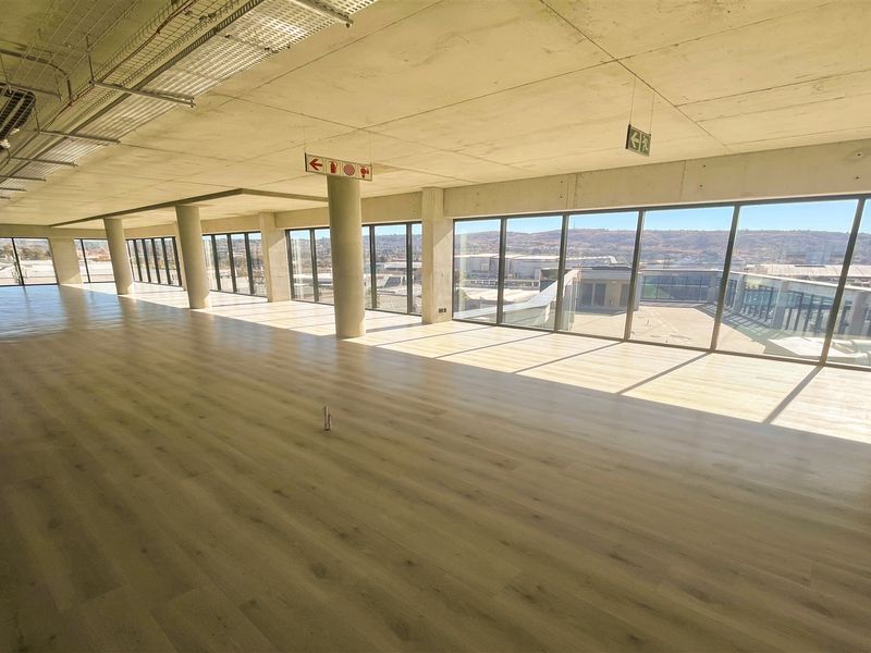 Spacious open-plan office area featuring modern laminate flooring, exposed concrete ceilings, and expansive floor-to-ceiling windows offering abundant natural light and views.