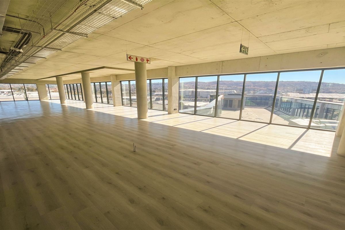 Spacious open-plan office area featuring modern laminate flooring, exposed concrete ceilings, and expansive floor-to-ceiling windows offering abundant natural light and views.