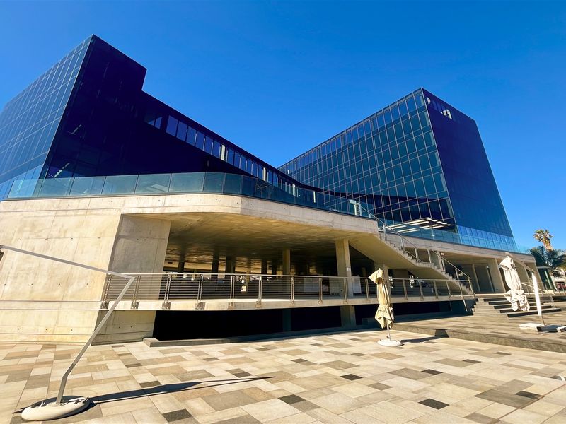 Modern commercial office building featuring a striking glass facade, concrete structural elements, and an expansive paved outdoor terrace area.