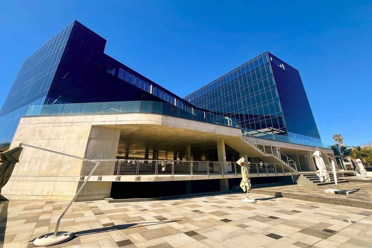 Modern commercial office building featuring a striking glass facade, concrete structural elements, and an expansive paved outdoor terrace area.