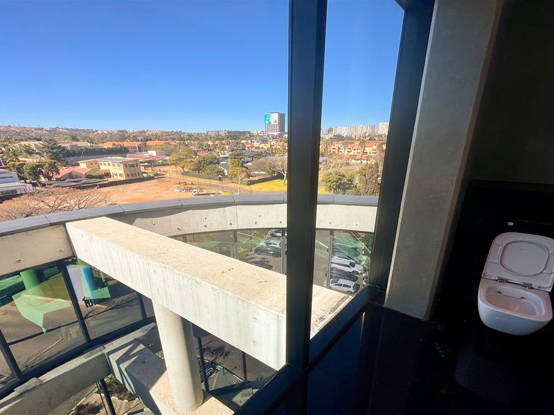 Modern bathroom featuring a wall-mounted toilet and expansive floor-to-ceiling windows offering panoramic urban views.