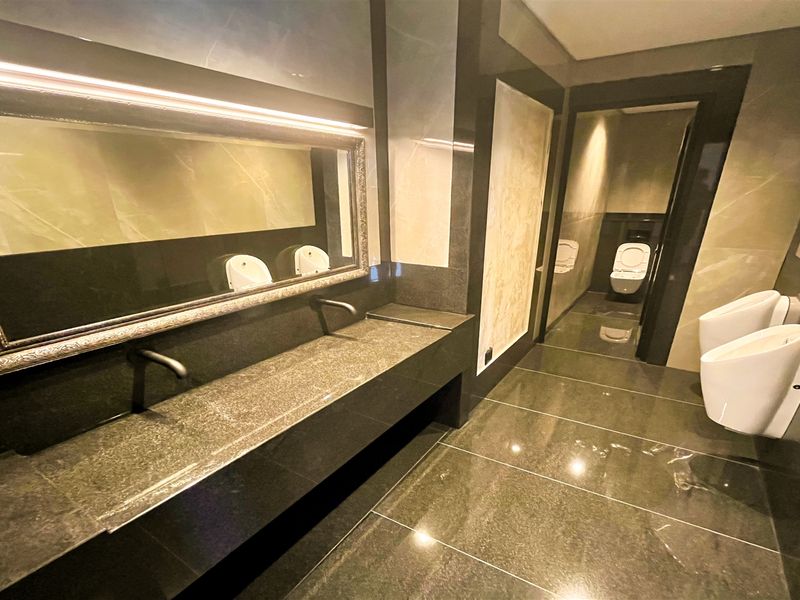 Modern office bathroom featuring high-end stone finishes, wall-mounted faucets, multiple urinals, and a private toilet cubicle with sleek, contemporary design.