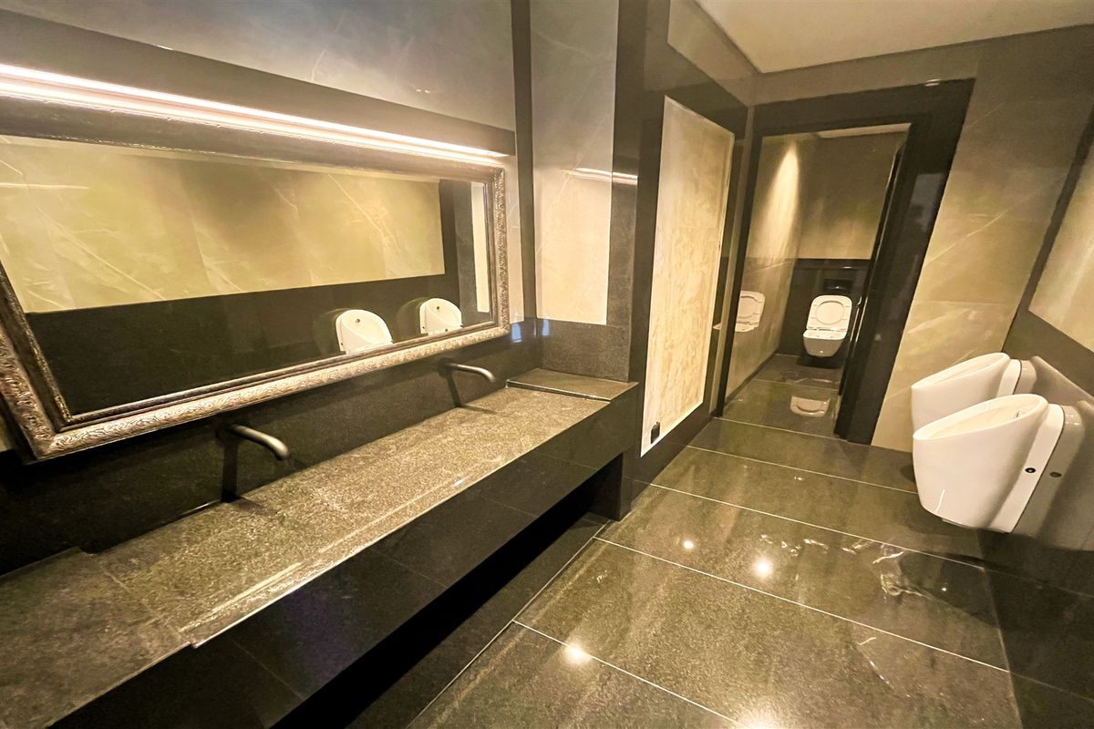Modern office bathroom featuring high-end stone finishes, wall-mounted faucets, multiple urinals, and a private toilet cubicle with sleek, contemporary design.