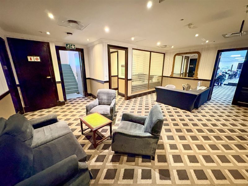 A professional office reception or waiting area featuring patterned carpeting, recessed lighting, and a glass partition wall.