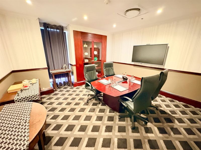 A professional office meeting room featuring a built-in display cabinet, wall-mounted screen, recessed lighting, and patterned carpeting.