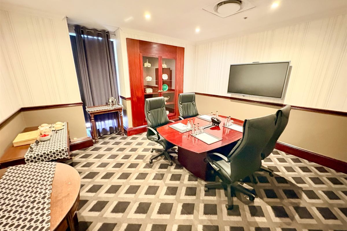 A professional office meeting room featuring a built-in display cabinet, wall-mounted screen, recessed lighting, and patterned carpeting.