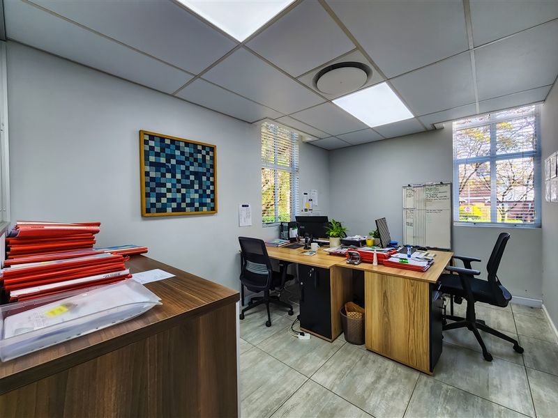 A functional office space featuring tiled flooring, a suspended ceiling with recessed lighting, and large windows with blinds providing natural light.
