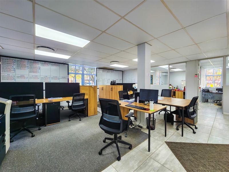 A functional open-plan office space featuring suspended ceilings, recessed lighting, glass partitions, and a mix of carpet and tile flooring.