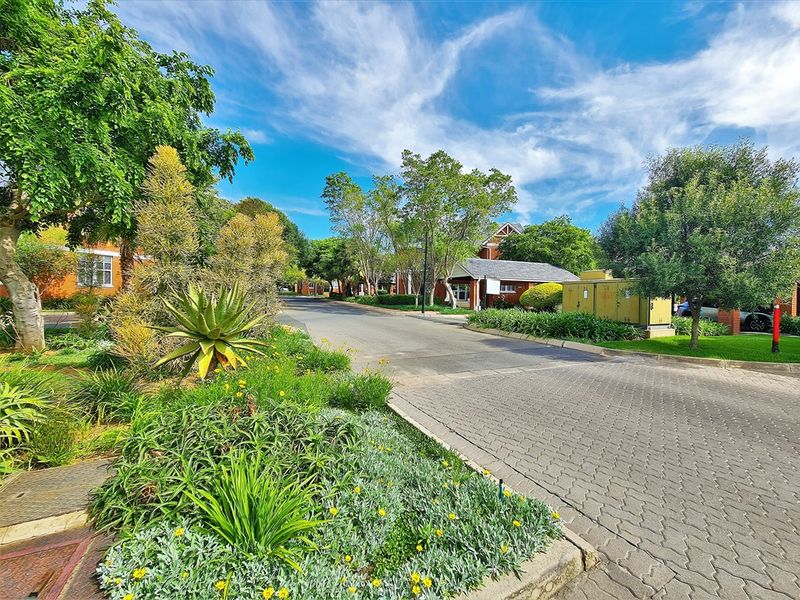 A well-maintained office park street view featuring paved access roads, mature landscaping, and established garden beds.