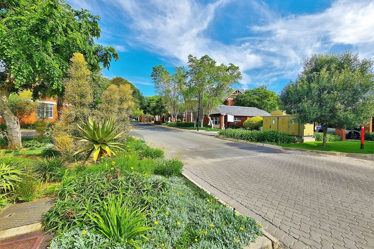 A well-maintained office park street view featuring paved access roads, mature landscaping, and established garden beds.