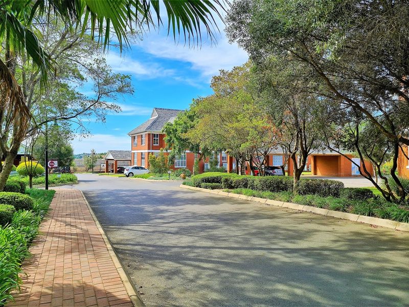 A well-maintained office complex featuring a red brick facade, paved walkways, and mature landscaped gardens with ample driveway and covered parking space.