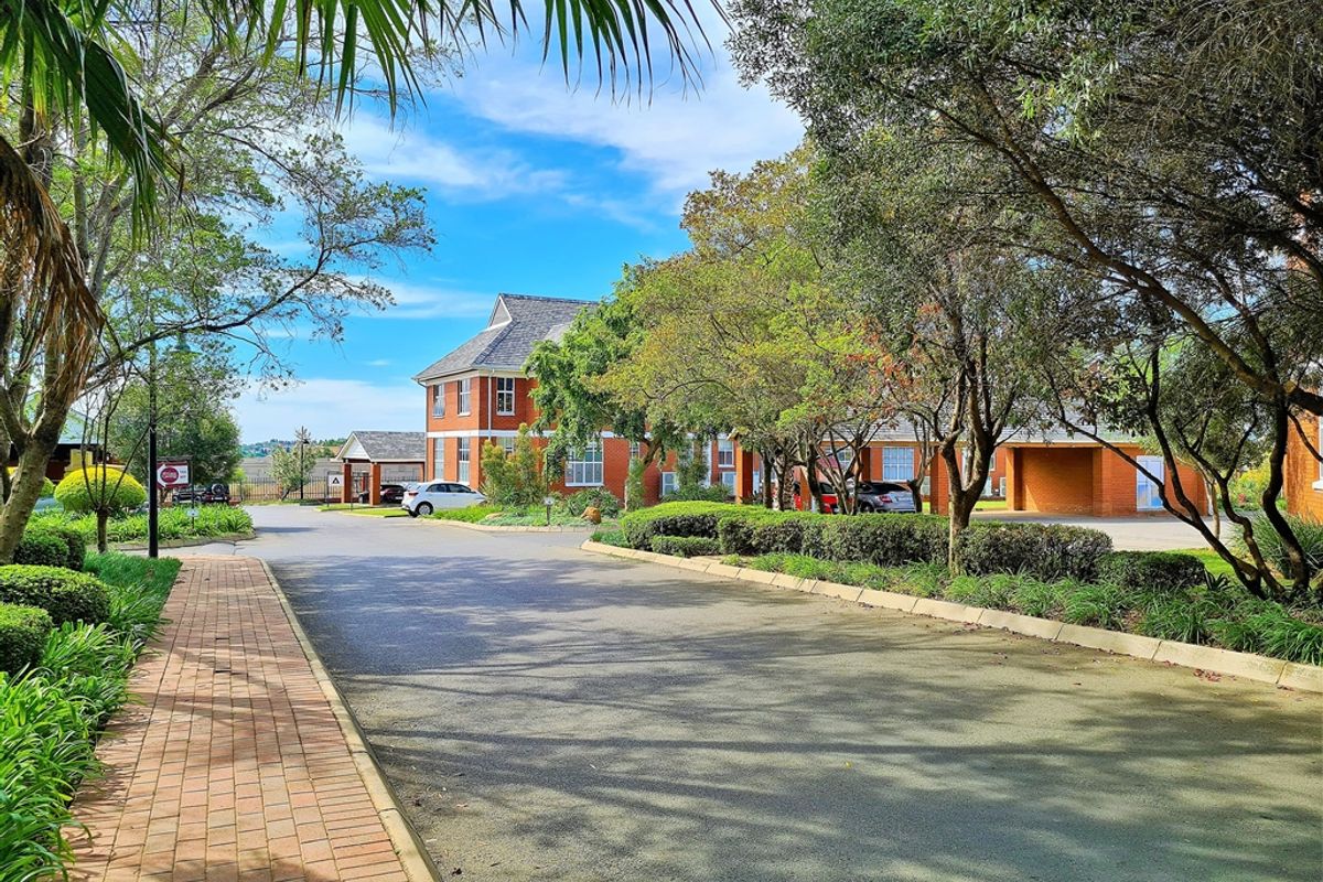 A well-maintained office complex featuring a red brick facade, paved walkways, and mature landscaped gardens with ample driveway and covered parking space.