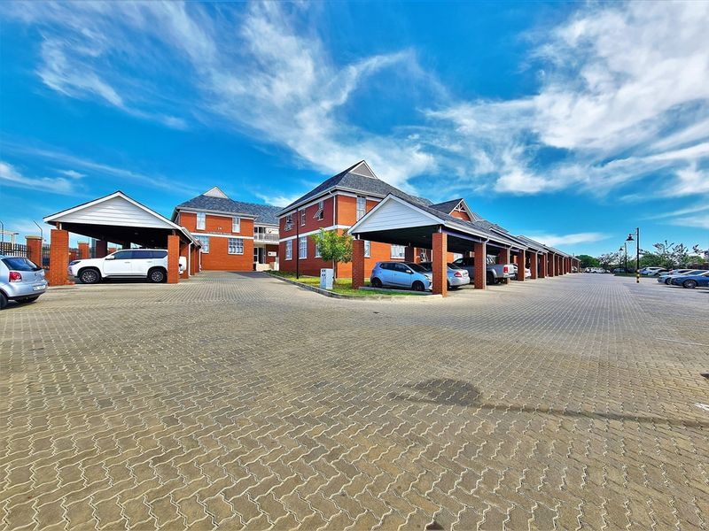 Exterior view of a professional office complex featuring red brick architecture, extensive paved parking areas, and covered parking bays.