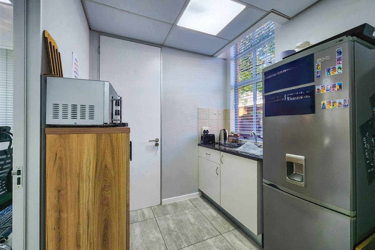 A compact office kitchenette featuring tiled flooring, built-in cabinetry, a sink, and a drop ceiling with recessed lighting.