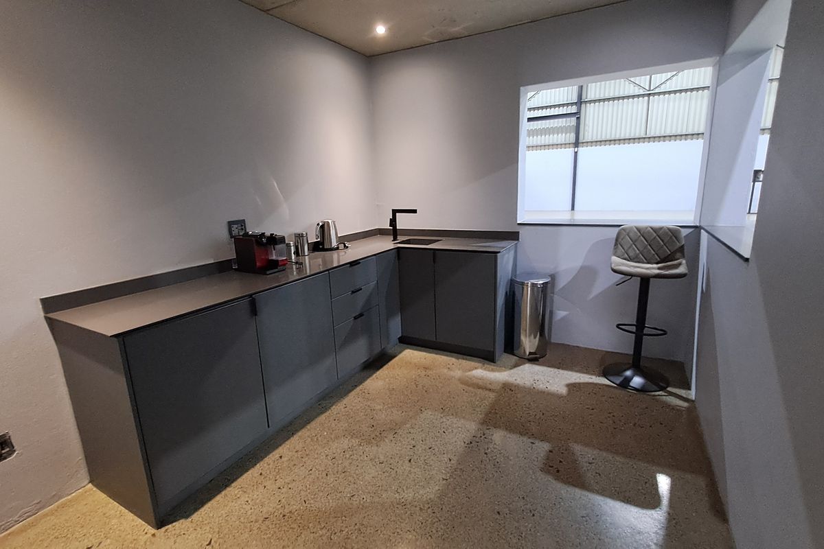 A modern industrial-style kitchenette featuring dark grey cabinetry, polished concrete floors, and a sleek integrated sink area.