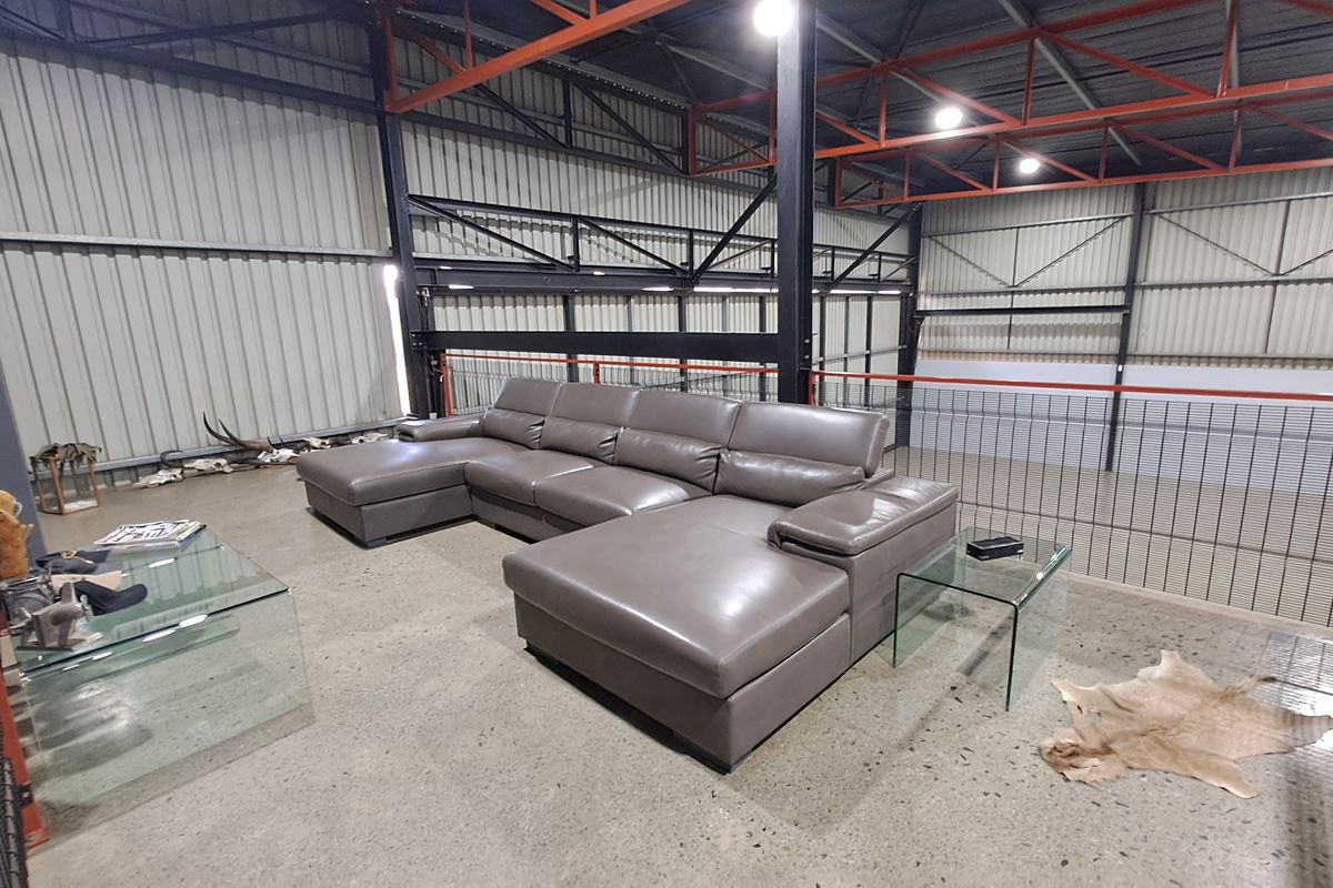 A spacious industrial-style mezzanine living area featuring exposed steel roof trusses, corrugated metal walls, and polished concrete flooring overlooking the warehouse space below.