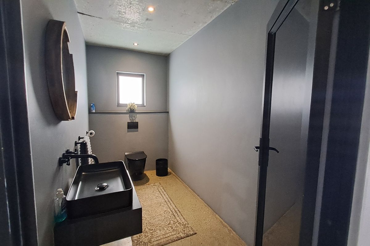 Modern industrial-style bathroom featuring a sleek black wall-mounted basin, wall-hung toilet, polished concrete flooring, and exposed concrete ceiling with recessed lighting.