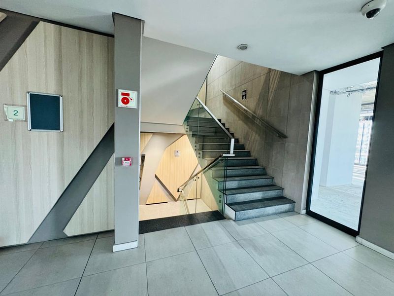 Modern office building entrance lobby featuring a contemporary staircase with glass balustrades, tiled flooring, and integrated fire safety systems.