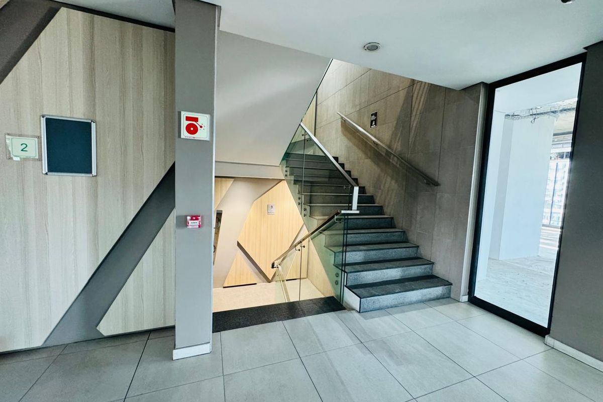 Modern office building entrance lobby featuring a contemporary staircase with glass balustrades, tiled flooring, and integrated fire safety systems.