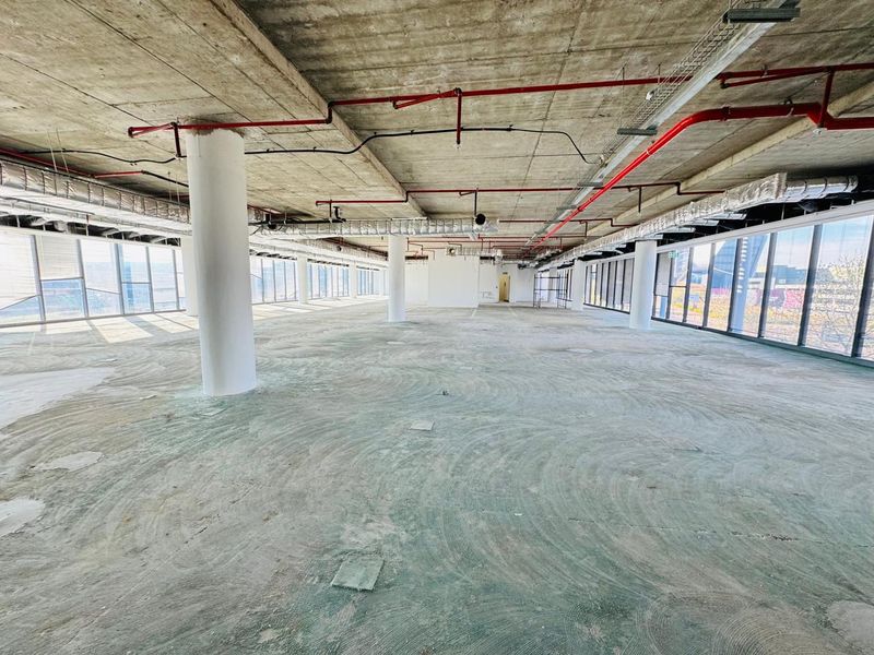 Expansive open-plan office space featuring floor-to-ceiling windows, exposed concrete ceilings, and industrial-style utility infrastructure, ready for custom fit-out.