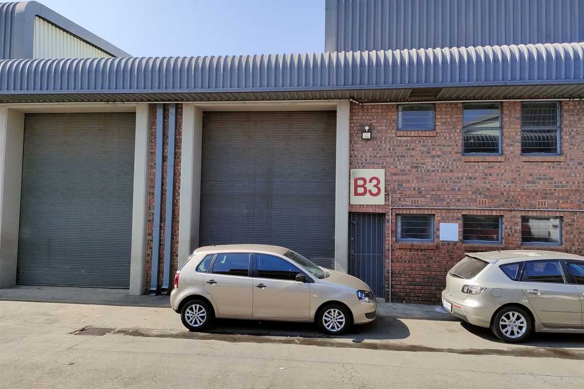 Industrial unit exterior featuring face brick facade, multiple roller shutter doors, and metal roofing, providing functional access for commercial or warehouse operations.