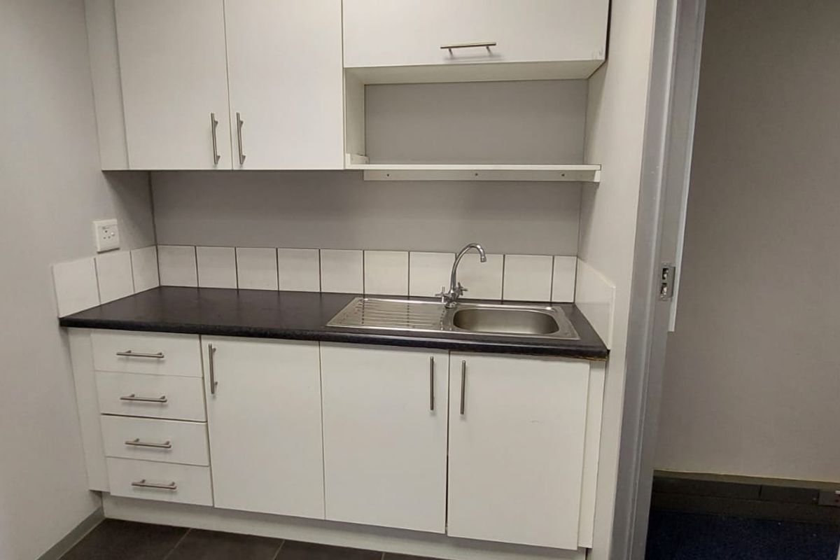 A compact kitchenette featuring white built-in cabinetry, a dark laminate countertop, and a stainless steel sink with a tiled splashback.