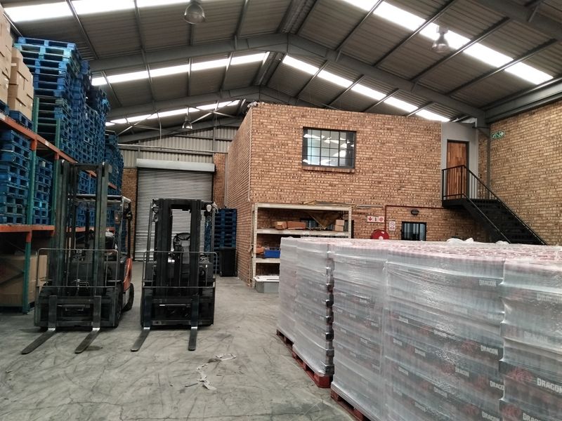 Spacious industrial warehouse featuring high ceilings with skylights, exposed brick walls, a mezzanine level with steel staircase, and a large roller shutter door.
