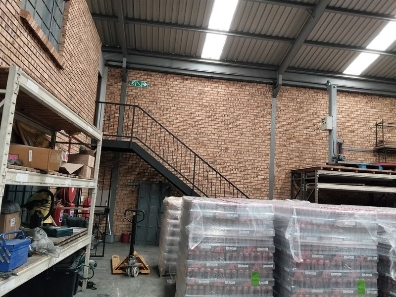 Industrial warehouse space featuring exposed brick walls, a steel staircase, and high-clearance metal roofing with integrated skylights for natural illumination.