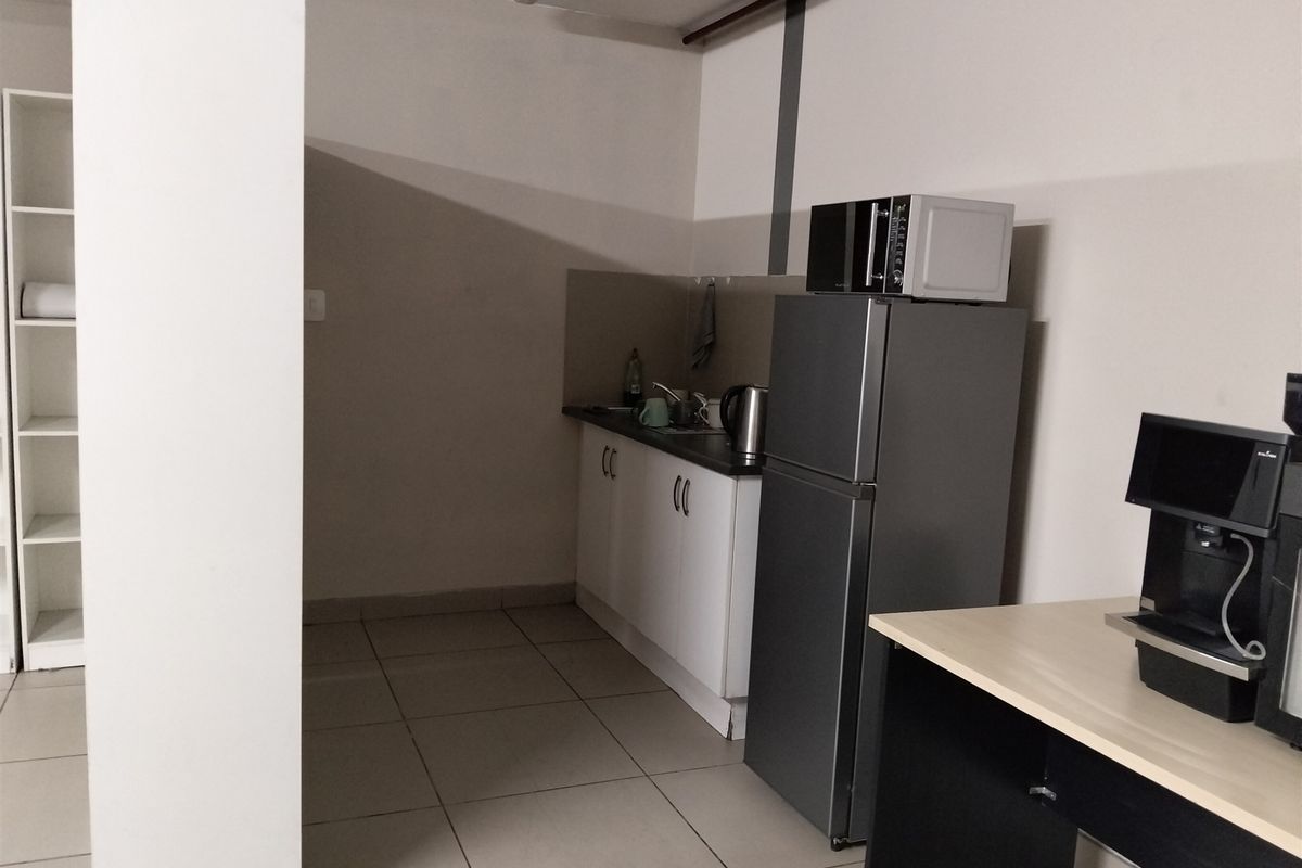 A functional kitchenette area featuring built-in cabinetry, a sink, and tiled flooring, suitable for office or industrial utility use.