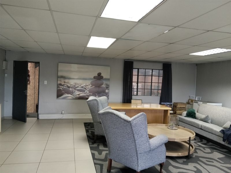 A spacious office or lounge area featuring a suspended ceiling with recessed lighting, tiled flooring, and a large steel-framed window.