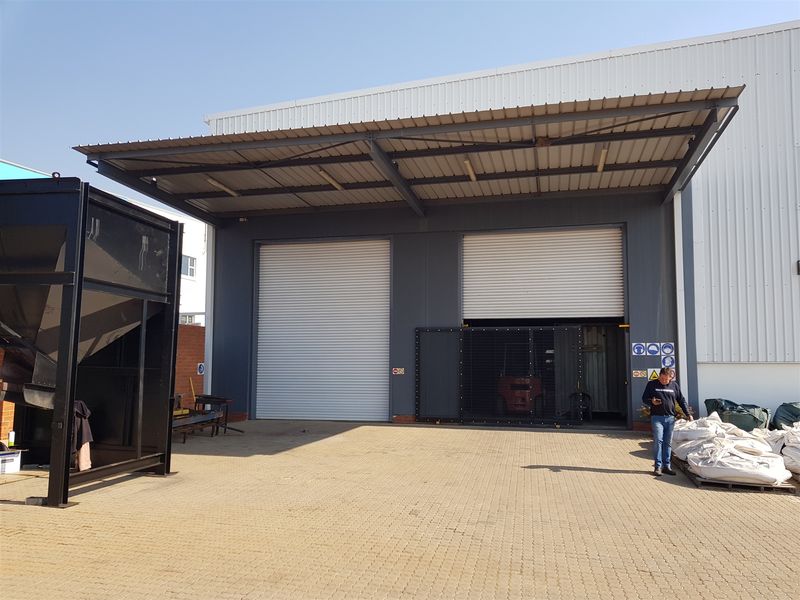 Industrial warehouse exterior featuring a paved yard, steel canopy, and dual roller shutter doors for efficient loading and access.