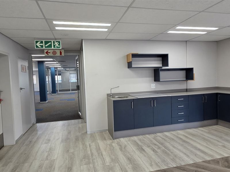 Modern office kitchenette area featuring built-in cabinetry, stainless steel sink, and durable laminate flooring, leading into an open-plan workspace.