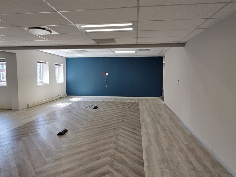 Spacious open-plan office area featuring modern herringbone vinyl flooring, a bold blue accent wall, and a clean suspended ceiling with recessed lighting.
