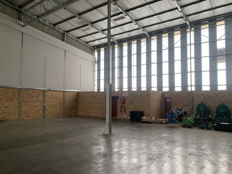 Spacious industrial warehouse unit featuring high ceilings, exposed steel trusses, clerestory windows for natural light, facebrick walls, and durable concrete flooring.
