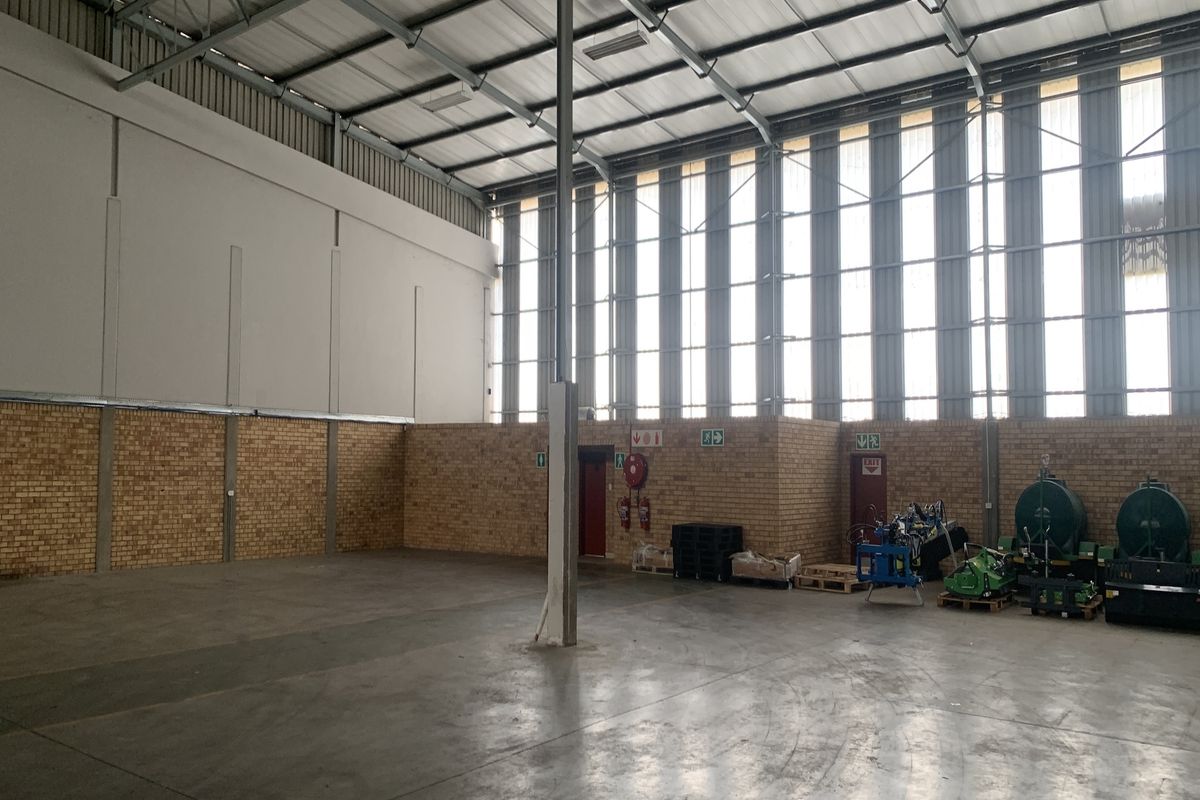 Spacious industrial warehouse unit featuring high ceilings, exposed steel trusses, clerestory windows for natural light, facebrick walls, and durable concrete flooring.